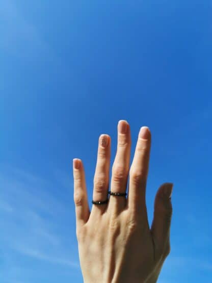 Na zdjęciu są pierścionki z obsydianów "Ochrona", na kobiecej dłoni na tle nieba.