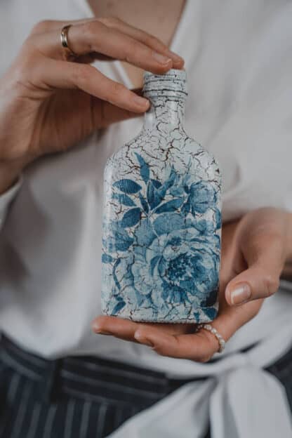 Na zdjęciu jest butelka decoupage w niebieskie róże.