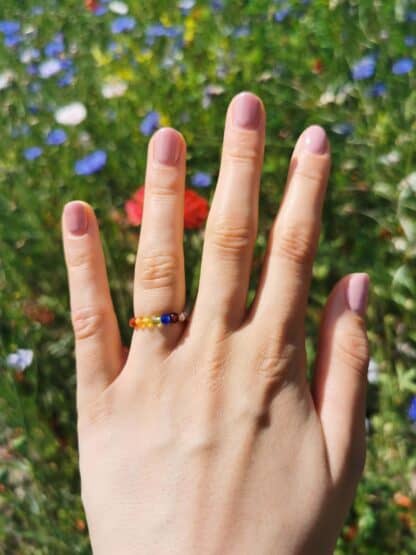 Na zdjęciu jest dłoń z tęczowym pierścionkiem Szczęśliwe Kolory