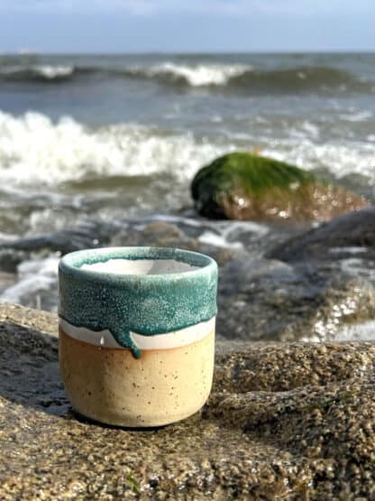 Na zdjęciu jest kubek ceramiczny-czarka w kolorach morskich, na tle morza.