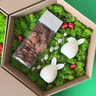 Na zdjęciu jest pudełko ze świecami i pierniczkami w kształcie zajączków na zielonym mchu: "zajączek - prezent wielkanocny"