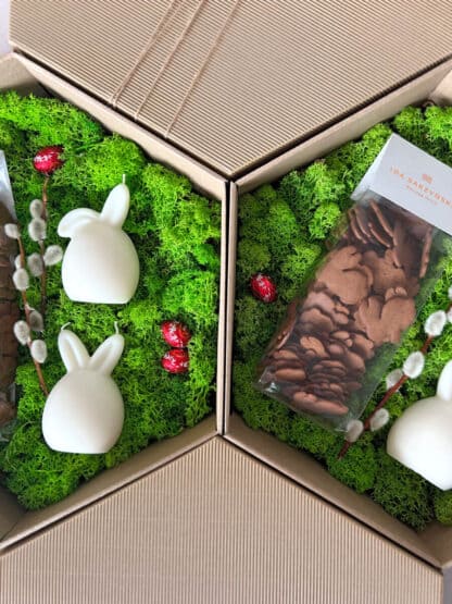 Na zdjęciu jest pudełko ze świecami i pierniczkami w kształcie zajączków na zielonym mchu: "zajączek - prezent wielkanocny"