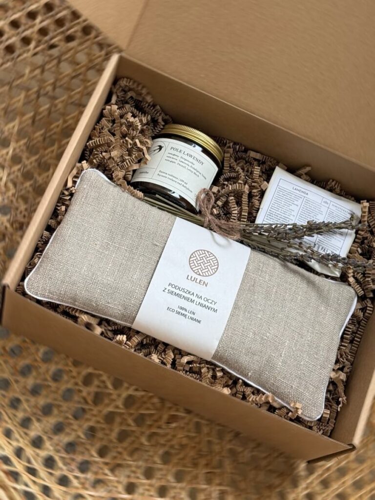Na zdjęciu jest prezent na odpoczynek "Lawendowy relaks" ze świecą sojową, półkulą kąpielową oraz poduszką na oczy z siemieniem lnianym.